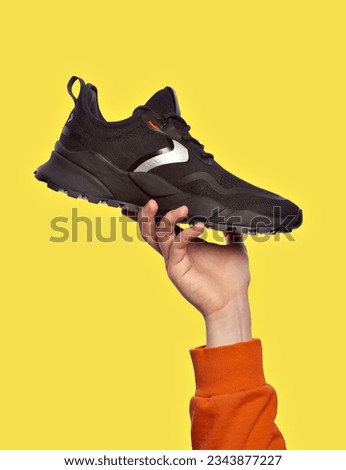 Stylish black sneaker presentation in a man's hand, isolated on a yellow background. Selling modern sports shoes. Advertising concept