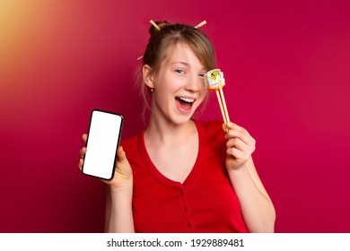 Stylish Blonde Girl Covering Eye With Sushi Roll, Red Studio Background With Space For Advertising. Pretty Female Holding Japanese Roll By Chopsticks, Mock Up Smartphone Screen For Online Info