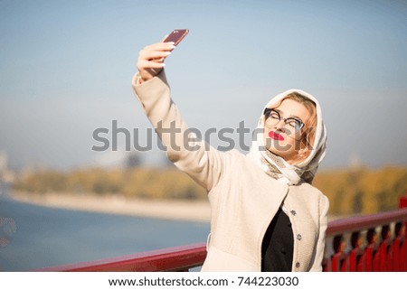 Stylish blonde woman tourist taking selfie on smart phone. Woman wears shawl and glasses