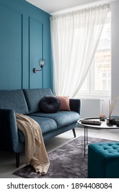 Stylish Blue Couch With Decorative Pillows, Black Coffee Table And Blue, Square Ottoman In Small Living Room With Window And Molding On Teal Blue Wall