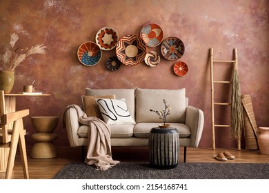 The stylish boho composition at living room interior with design beige sofa, coffee table, wicker baskets and elegant personal accessories. Brown and white pillows and plaid Cozy apartment. Home decor - Shutterstock ID 2154168741