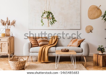 The stylish boho compostion at living room interior with design gray sofa, wooden coffee table, commode and elegant personal accessories. Honey yellow pillow and plaid. Cozy apartment. Home decor