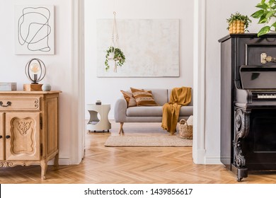 The stylish boho interior of living room in cozy apartment with design coffee table, gray sofa, honey yellow pillows, piano, wooden shelf, plants and elegant personal accessories. Mock up paintings.