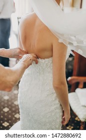 Stylish bride getting dressed in modern gown with bridesmaids and mom in hotel room. Morning preparation before wedding ceremony. Mother helping daughter get dressed - Shutterstock ID 1472880692