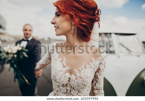 stylish bride and groom
holding hands, smiling and walking near retro car with boho
bouquet. luxury wedding couple newlyweds, sensual emotional moment.
space for text.