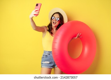 Stylish brunette girl on vacation, taking selfie with swim ring, going on beach, swimming in sea on summer holiday, standing over yellow background - Powered by Shutterstock