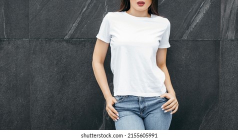 Stylish Brunette Girl Wearing White T-shirt, Blue Jeans And Glasses Posing Against Street , Urban Clothing Style. Street Photography