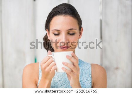 Stylish brunette holding a mug against bleached wooden fence