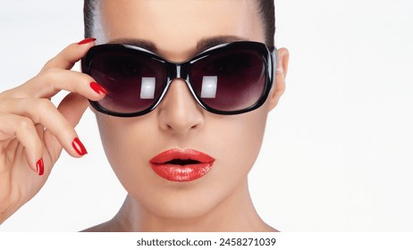 Stylish brunette model posing confidently with black oversized sunglasses. Emphasizing vibrant nail polish and glossy lips, isolated on white background with copy space. - Powered by Shutterstock