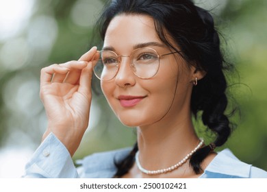 Stylish brunette woman wearing glasses, posing outdoors in a serene natural setting. Perfect for themes of fashion, nature, and modern lifestyle. High quality image for advertisements and promos. - Powered by Shutterstock