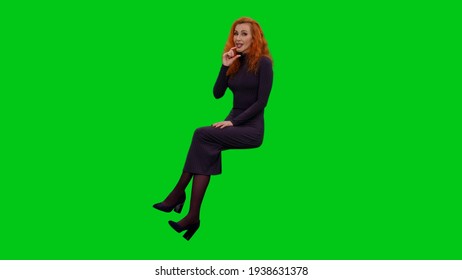 Stylish Business Woman In Long Dress Sitting While Telling Story And Gesturing On Green Screen Background