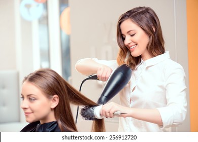 Stylish by professionals you can trust.  Mirror reflection of a young beautiful hairdresser doing her clients hair with a hair drier on the background of the hairdressing salon  - Shutterstock ID 256912720