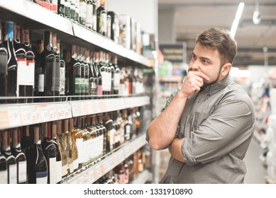 Stylish Casual African American Man At Jeans Jacket And Black Beret Holding Basket And Looking On Bottle Of Wine, Shopping At Supermarket.