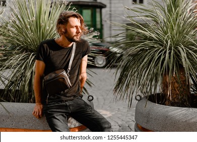 Stylish casual american man in black t shirt and jeans with waist bag in the summer city street.