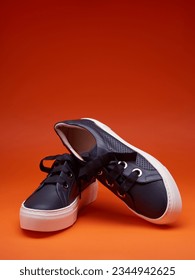 Stylish casual navy blue sneakers with thick white soles and wide shoelaces, isolated on a bright red-orange background with copy space for text. Advertising poster, shoe sale, fashion photography