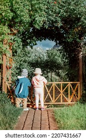 Stylish Caucasian Kids Playing In  The Green Spring Garden With The Hats On Their Heads. Little Boy And Little Girl In A Magical Garden.