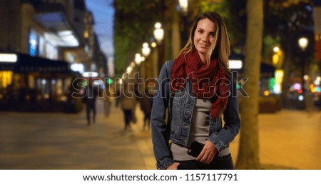 Stylish Caucasian woman on the Champs-Elysees at night smiling at camera