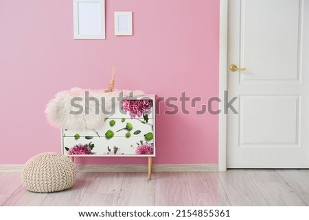 Stylish chest of drawers with reed diffuser and pouf near pink wall