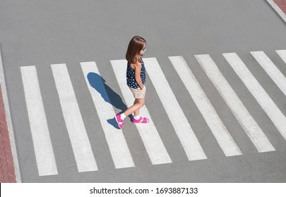 Stylish Child In Fashion Clothes Is Walking Along Summer City Crosswalk. Kid On Pedestrian Side Walk. Concept Pedestrians Passing A Crosswalk. Traffic Rules. From Top View. Shadow At Zebra Crossing