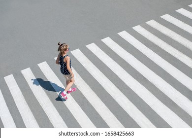 Stylish Child In Glasses, Fashion Clothes Walking Along Summer City Crosswalk. Kid On Pedestrian Side Walk. Concept Pedestrians Passing A Crosswalk. From Top View. Behind. Shadow At Zebra Crossing