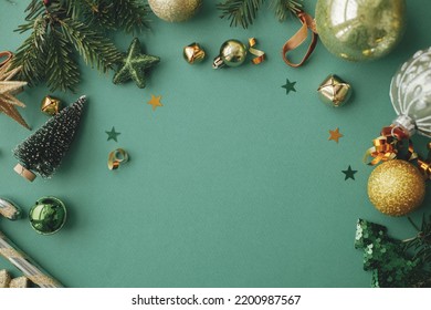 Stylish christmas flat lay with golden festive decorations, confetti, gift, fir branches on green background. Seasons greetings card template, space for text. Merry Christmas and Happy Holidays!