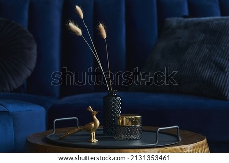 Stylish close up on the elegant details in the glamour living room interior. Golden peacock and creative personal accesories. Dark blue sofa on the background. Template. Copy space.