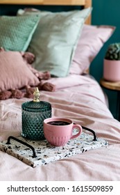 Stylish composition of bedroom interior with lastrico tray with coffee and elegant personal accessories. Beautiful pink and green bed sheets, blanket and pillow. Template Design home staging. Close up