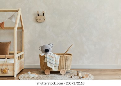 Stylish composition of cozy scandinavian child's room interior with bed, rattan basket, plush and wooden toys and textile hanging decorations. Creative wall, carpet on the floor. Copy space. Template.