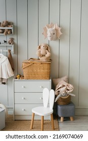 A stylish composition of a cozy Scandinavian interior of a children's room with a chair with bunny ears, plush and wooden toys, a rattan basket on the chest of drawers and textile hanging flags