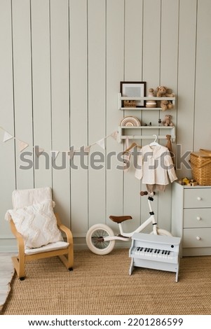 Stylish composition of a cozy Scandinavian interior of a children's room with an armchair, plush and wooden toys, a rattan basket on the chest of drawers and textile hanging flags