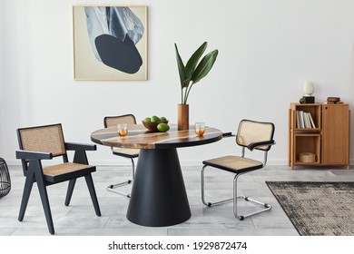Stylish composition of dining room interior with design table, modern chairs, decoration, tropical leaf in vase, fruits, bookcase, abstract mock up paintings and elegant accessories in home decor.