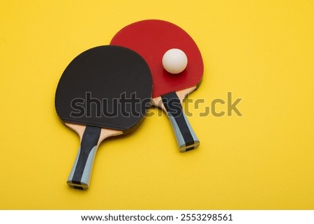 Stylish composition featuring two professional ping pong paddles with red and black rubber surfaces, accompanied by white competition ball, arranged on vibrant yellow backdrop