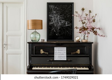 Stylish composition at living room interior with black piano, mock up poster map, dried flowers, clock, book, lamp, white wall and elegant presonal accessories in modern home decor.