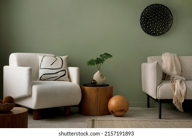 Stylish composition of living room interior with green wall, grey sofa with pillow. White armchair with brown pilow, wooden coffe table with leaves in beige vase, wooden ball. Black ornament on wall. 
