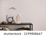 The stylish composition of minimalistic interior with copy space.  Black commode, vase with dried flowers, sculpture and personal accessories. Beige wall. Home decor. Template. 