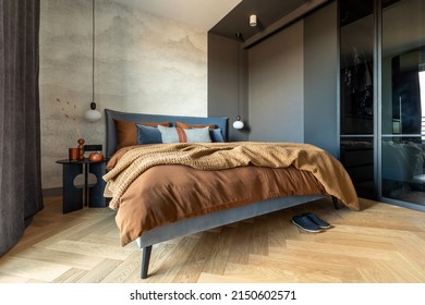 Stylish Composition Of Modern Bedroom Interior. Bed, Creative Lamp And Elegant Personal Accessories. Concrete Wall. Brown Sheeets. Minimalistic Masculine Concept. Template.
