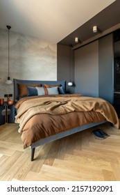 Stylish Composition Of Modern Bedroom Interior. Bed, Creative Lamp And Elegant Personal Accessories. Concrete Wall. Brown Sheeets. Minimalistic Masculine Concept. Template.