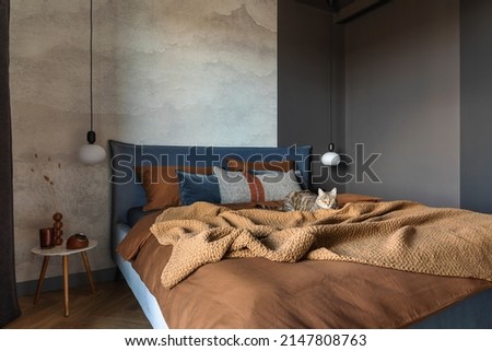 Stylish composition of modern bedroom interior. Bed, creative lamp and elegant personal accessories. Concrete wall. Brown sheeets. Minimalistic masculine concept. Template.