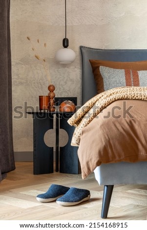 Stylish composition of modern bedroom interior. Bed, creative lamp and elegant personal accessories. Concrete wall. Brown sheeets. Minimalistic masculine concept. Template.