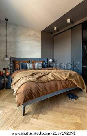 Stylish composition of modern bedroom interior. Bed, creative lamp and elegant personal accessories. Concrete wall. Brown sheeets. Minimalistic masculine concept. Template.