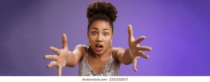 Stylish confused african woman in silver shiny dress cringing worried extend arms forward concerned standing perplexed panicking falling during night club, standing blue background. Copy space - Powered by Shutterstock