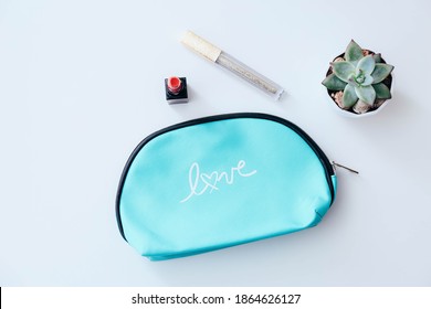Stylish cosmetic bag, listick, lip gloss and succulent on white table background, top view