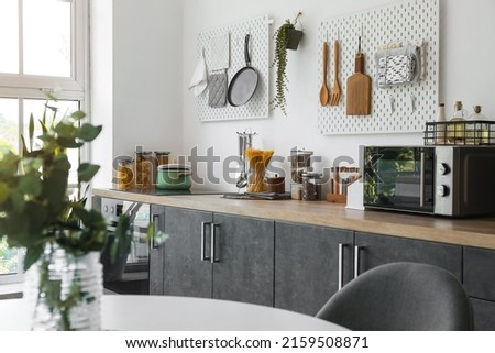 Stylish counters with utensils and pegboards on light wall in kitchen