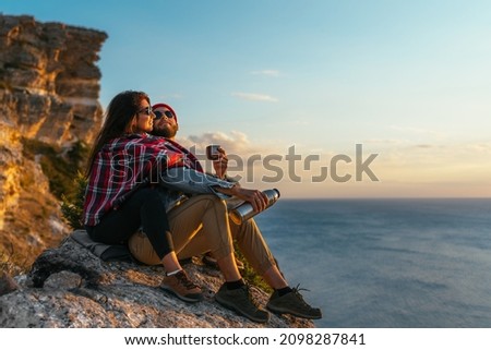 A stylish couple admires the seascape at sunset. A couple in love at sunset by the sea. A man and a woman are traveling. A beautiful couple meets the sunset on the seashore. Couple on the cape