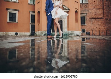 Stylish Couple Dancing In European City Street On Background Of Old Architecture And Reflection In Water. Fashionable Man And Woman In Love Dancing. Traveling Together In Europe