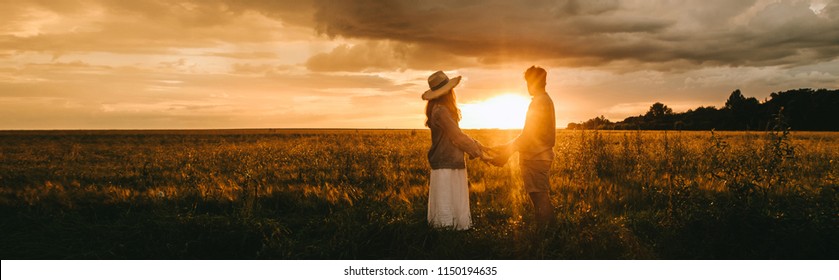 stylish couple holding hands on meadow at beautiful sunset with back light, love story