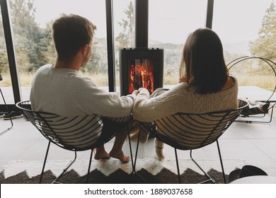 Stylish Couple In Sweaters Relaxing Together At Modern Black Fireplace With View On Mountains. Cozy Warm Family Moments At Cold Season. Young Family On Vacation