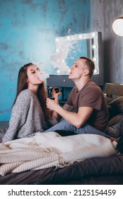 Stylish couple vaping in bed. Two people use the electronic cigarette