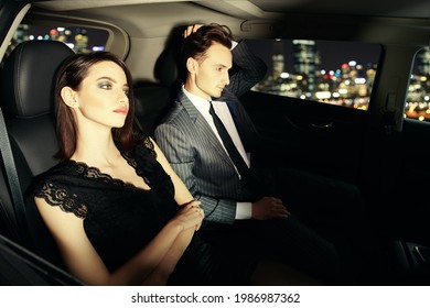 Stylish Couple Of Young People In Evening Dresses Driving Through The City At Night. Glamorous Lifestyle, Night Party. Evening Fashion. 