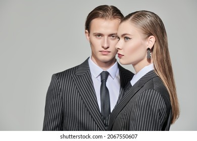 Stylish couple of young people man and woman in elegant striped pantsuits. Studio portrait on a gray background. Impeccable look. Fashionable business style.